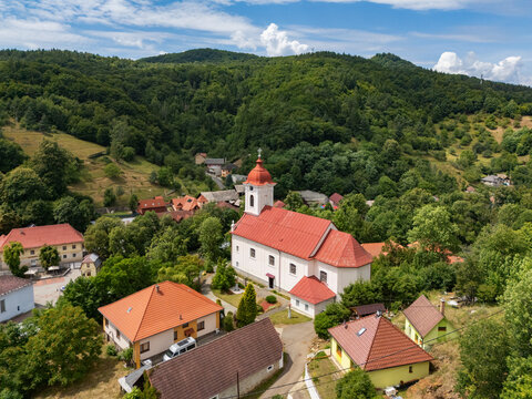Aerial view of the Church of St. Luke with its vibrant red roof and the surrounding lush green trees creating a picturesque scene, Sklene Teplice, Banska Bystrica Region, Slovakia.