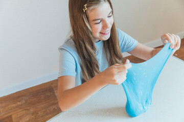 Young girl happily stretching a wide, elastic sheet of bright blue slime. Fun sensory game and creative DIY hobby
