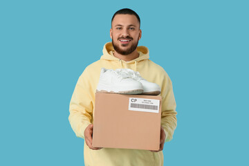 Young man with parcel box and new sneakers on blue background