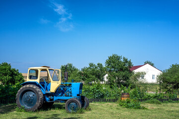 A tractor stands next to a rural house surrounded by plants and greenery in Hacihetemli, Azerbaijan.