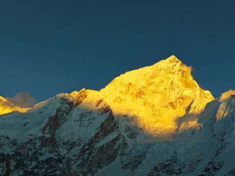 Majestic snow-capped mountain peak illuminated by golden sunlight against a clear blue sky, showcasing the beauty of nature and the grandeur of the landscape