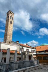 Fototapeta premium Vertical view of a historic clock tower rising above a cemetery in Sarajevo, Bosnia and Herzegovina, showing layers of religious history and urban heritage.