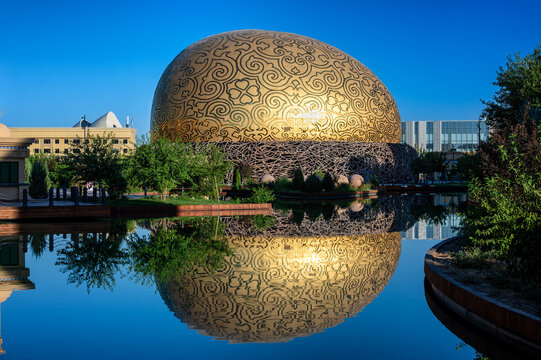 TURKESTAN, KAZAKHSTAN - JULY 17, 2025: Modern Samruk Flying Theater building reflected in water in Turkestan, Kazakhstan, creating a symmetrical architectural composition.