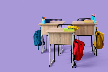 Modern school desks with backpacks and stationery on lilac background
