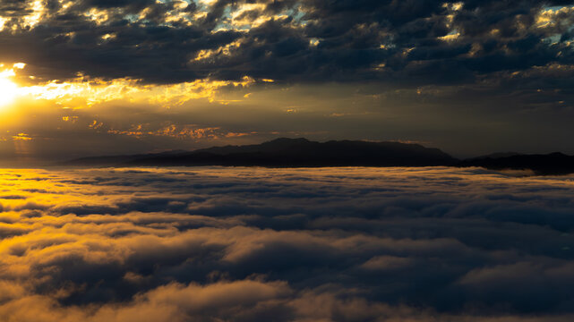 Aerial view of a golden sunset over a sea of clouds, with silhouetted mountains in the distance, Santa Monica, California, United States.