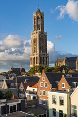 Vertical shot of the Dom Tower in Utrecht, Netherlands, illuminated by golden sunlight, standing tall above traditional Dutch houses.