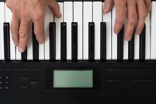 Closeup of male musician playing on digital synthesizer at home. Overhead view of hands playing electronic keyboard, home practice.