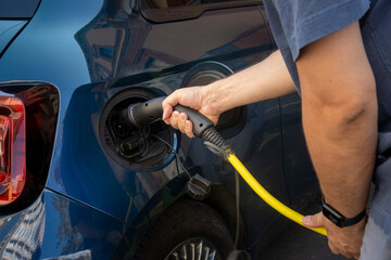 Person charging electric vehicle with yellow power cable in urban setting