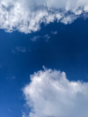 A vibrant and dramatic vertical view of a deep, rich blue sky framed by bright, fluffy white cumulus clouds. The image captures the natural beauty of a clear sunny day
