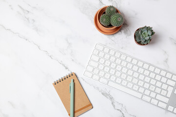 Top view of white keyboard, notebook and cactus on marble background in clean horizontal flatlay with wide copy space. Concept of clean workspace and creativity