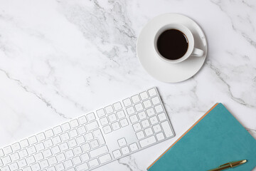 Top view horizontal of coffee cup, white keyboard and turquoise notebook on marble background with copy space, clean minimalist workspace style. Concept of modern workspace and creative lifestyle