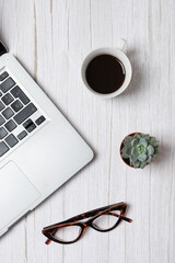 Top view vertical of laptop, coffee cup, glasses and succulent on light wood background, natural minimalist workspace aesthetic. Concept of modern workspace and creative lifestyle