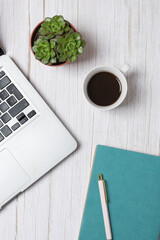 Top view vertical of laptop, coffee cup, succulents and turquoise notebook on light wooden background, clean and minimal composition. Concept of modern workspace and lifestyle