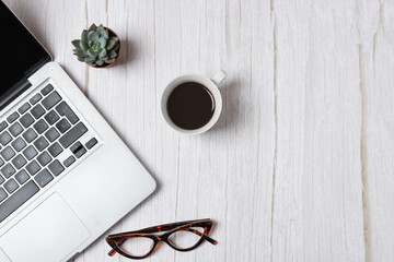 Top view horizontal of laptop, coffee cup, eyeglasses and succulents on light wooden background with ample copy space, clean minimal office style. Concept of modern workspace and lifestyle