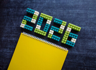 Colorful building blocks forming the numbers 2026 with notebook against a dark table. Perfect for celebrating New Year's Eve or welcoming the new year with festivities