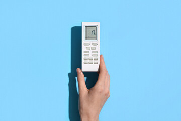 Female hand with air conditioner remote control on blue background