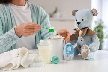 Woman preparing baby milk formula at table in kitchen, closeup