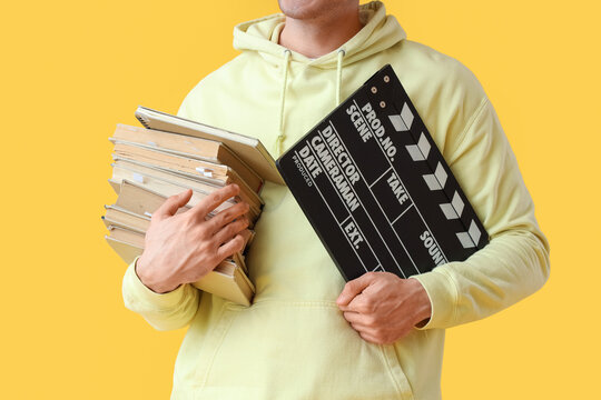 Male screenwriter with books and movie clapper on yellow background