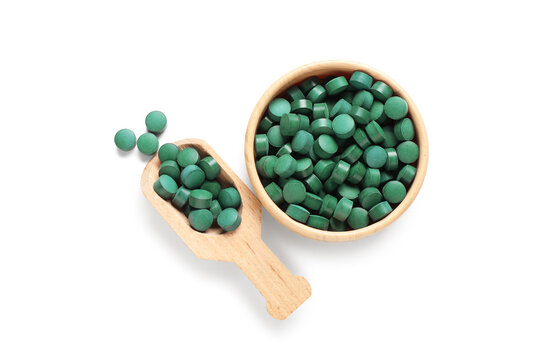 Bowl of spirulina tablets with wooden scoop on white background