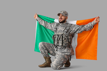 Young soldier with flag of Ireland on grey background