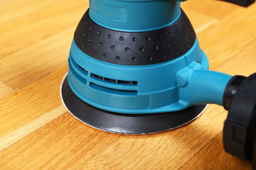 Sanding a wooden floor using an electric sander in a bright room.