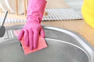 Female hand with sponge cleaning sink in kitchen, closeup