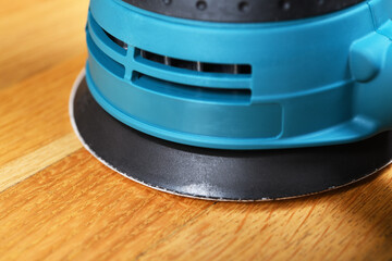 Sanding a wooden floor using an electric sander in a bright room.