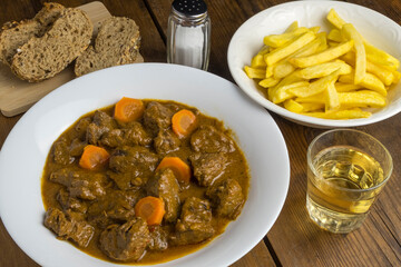 Carne en salsa con patatas fritas y vaso de vino blanco
