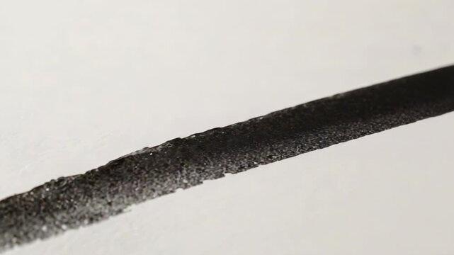 Showing black ink stroke drying from warm light after deposition and settling into textured paper