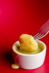 Gnocchi dipped in green pesto or cheese sauce with a fork against a vibrant red background. This food photography highlights Italian cuisine, taste, and gourmet dining with vibrant colors and close-up