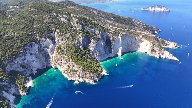 Aerial drone cinematic video of limestone white cliffs surrounded by deep blue emerald crystal clear sea and sea caves creating a true paradise for yachts and sailboats in tropical exotic island bay