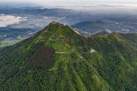 Aerial view of the lush green Telomoyo Mountain, its winding roads etched against the vibrant landscape, reaching towards the sky, Magelang, Central Java, Indonesia.