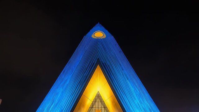 Zooming camera tilting toward apex at night, revealing blue LEDs, golden glass doors, sun emblem
