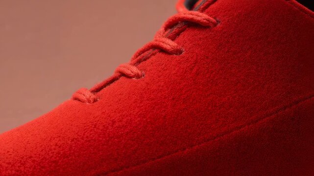 Shifting camera on play revealing red suede laced shoe in studio, showing stitched seam and eyelets