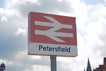 Petersfield Station Sign with National Rail Logo Against Cloudy Sky and Distant Buildings