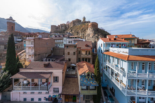 Aerial view of the Narikala fortress perched atop a rugged hill, overlooking a colorful cityscape with buildings and balconies, Tbilisi, Tbilisi, Georgia.