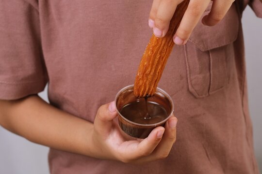 Closeup of a churro dipped into a chocolate cup, highlighting a delicious and crunchy dessert moment.