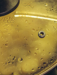 Close-up of steam and droplets forming on a glass saucepan lid with a yellow light reflection.