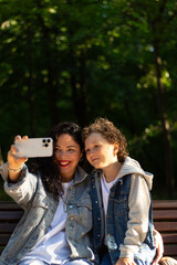 Young Caucasian mother and playful adorable little kid son making selfie photo or recording funny video, entertaining in public park