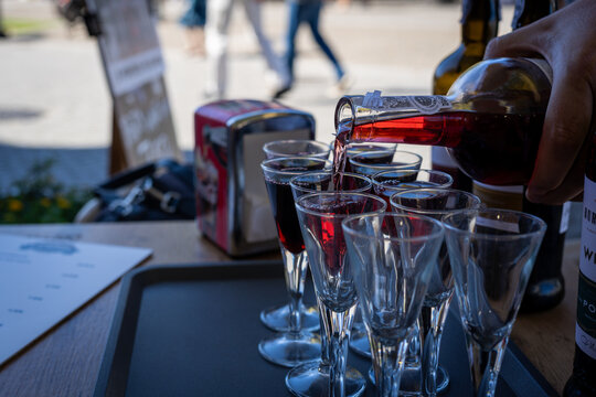 Pouring red wine into small glasses on a tray, ready for a tasting
