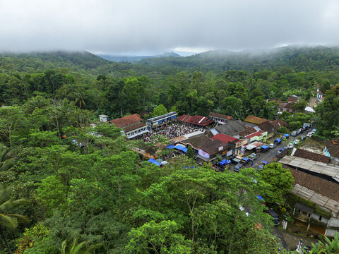 Aerial view of the bustling Kaligesing goat market nestled amidst green forests and hills under a misty sky, Purworejo Regency, Central Java, Indonesia.
