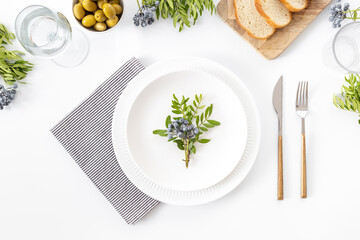 Festive table setting with empty plate, cutlery and napkin - green leaves decorated, bread and olives for dinner, flat lay. Top view