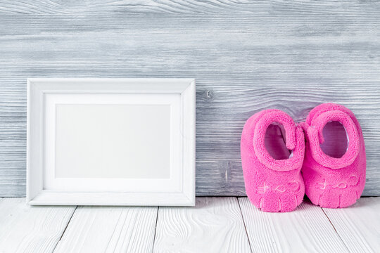 pink booties and photo frame on wooden background