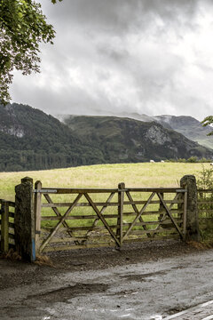 View of a wooden gate standing before a vast field leading up to green hills under a moody sky, Lake District, England, United Kingdom.