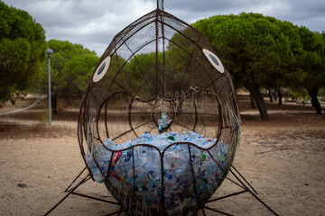 Fish-shaped trash receptacle filled with plastic bottles in a park setting