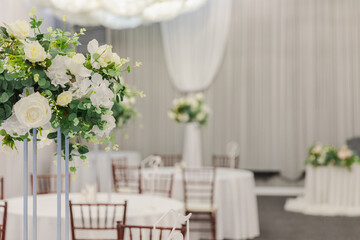 Decorated interior for festive event. Fancy table set for dinner with white flower composition in restaurant, luxury interior background. Wedding elegant banquet decoration arranged by catering