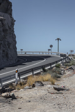 View of the winding asphalt road curves along the rugged coastline, where arid landscape meets a clear sky, creating a striking contrast of colors, Gran Canaria, Canary Islands, Spain.