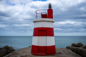 Striking red and white lighthouse stands tall against a cloudy sky near the ocean