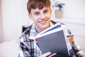A teenage boy in a checkered shirt unpacks notebooks and school books from his backpack after coming home from school. A bright and relatable lifestyle scene of everyday student life.
