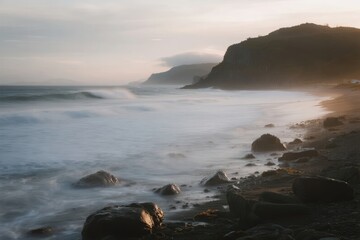 Coastal landscape with rocky shoreline and misty ocean waves at dawn